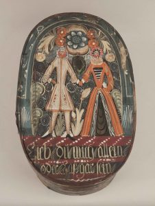 Antique Scandinavian painted oval bride's box. There is a depiction of a male and female figure on the lid. There are multiple colors, including orange, red, tan, and a greenish-blue.