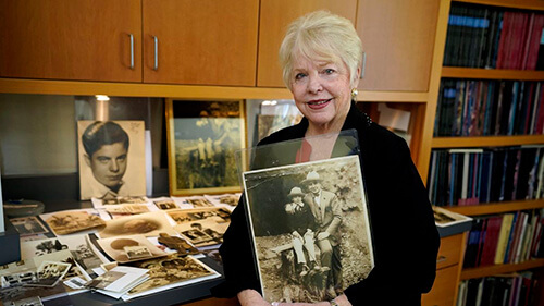 Al Capone's granddaughter, Diane, holding an old photograph of her father as a young boy sitting next to Al Capone. She is standing in front of a collection of old photographs of Al Capone and their family.