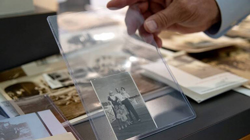 Close-up of a person's hand holding up a black and white family photo of Al Capone. It is encased in a clear protective cover.