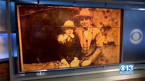Screenshot from a news program. There is an image of Al Capone sitting with his young son displayed on a set of nine television monitors to form one large monitor.